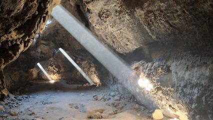 A cave with sunlight shining through small openings.