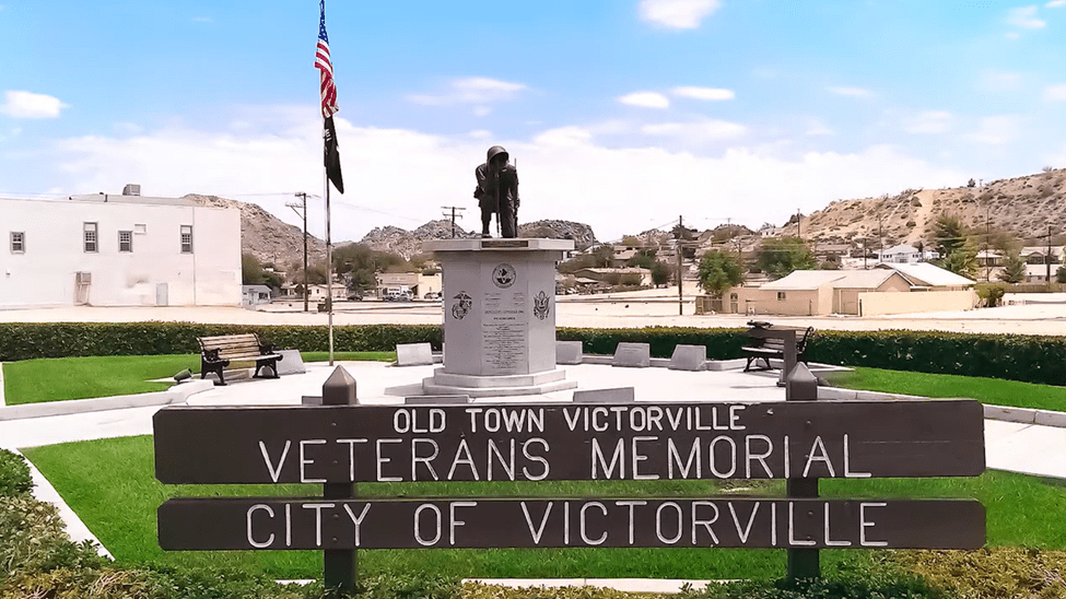 The Old Town Victorville Veterans Memorial featuring a statue and an American flag surrounded by grass.