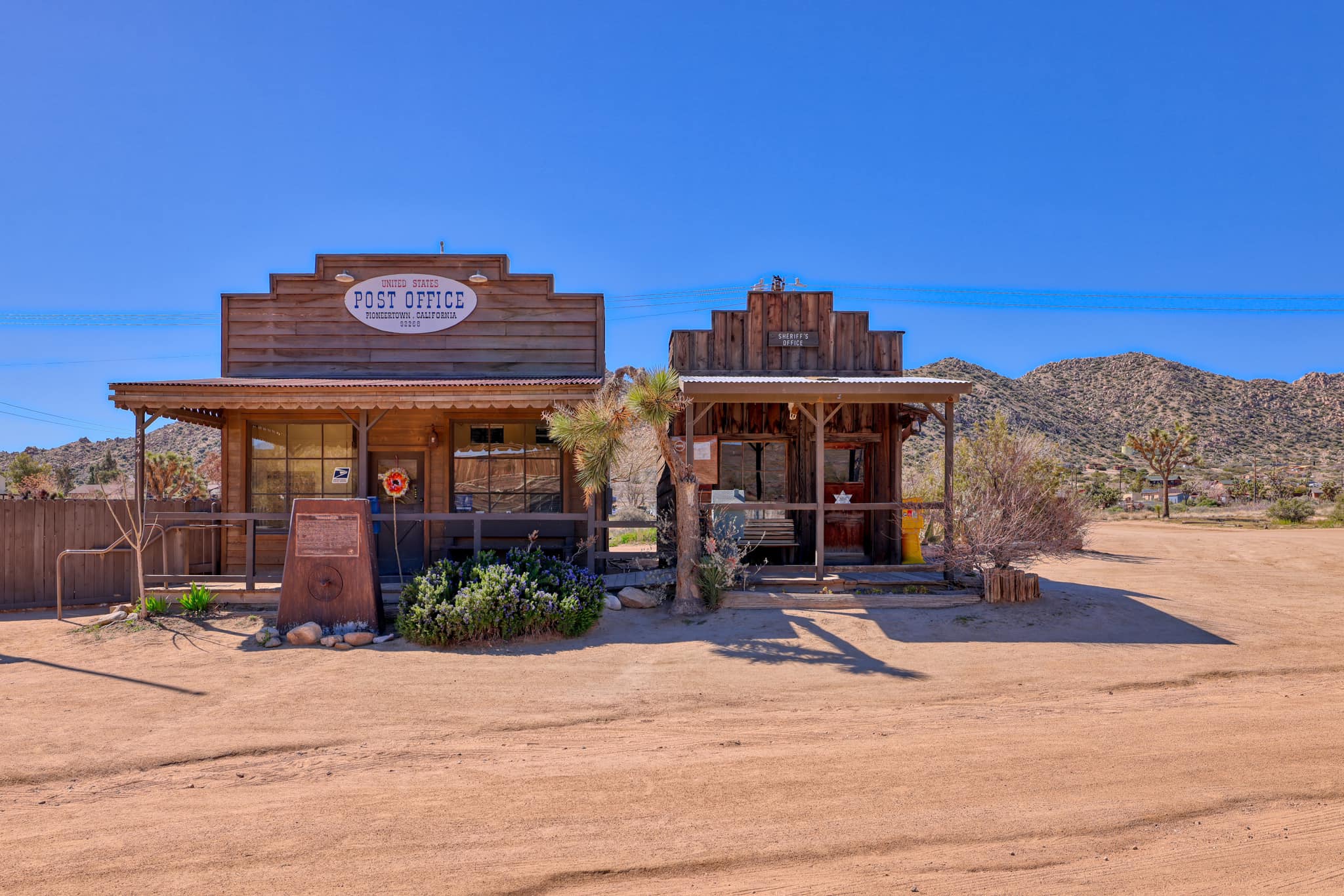 View of a rustic Old West-themed post office and another building next door, surrounded by desert landscape.