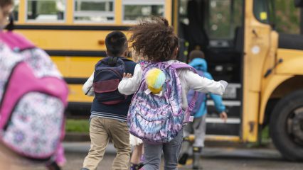 Children walking toward a school bus, used to emphasize preventing illness spread by keeping sick children home.