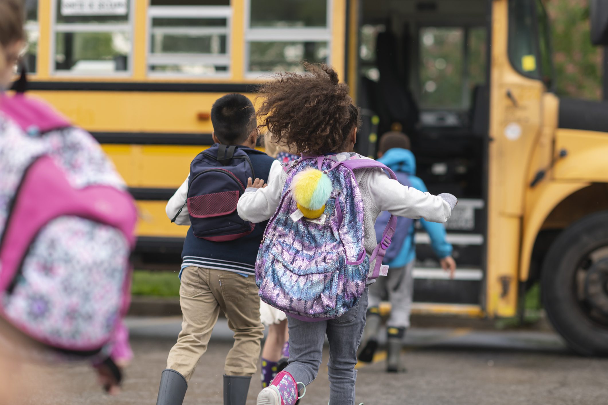Children walking toward a school bus, used to emphasize preventing illness spread by keeping sick children home.