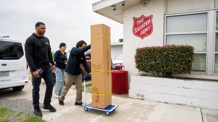 Three individuals transport a bed bug treatment unit on a cart outside of the Salvation Army building.