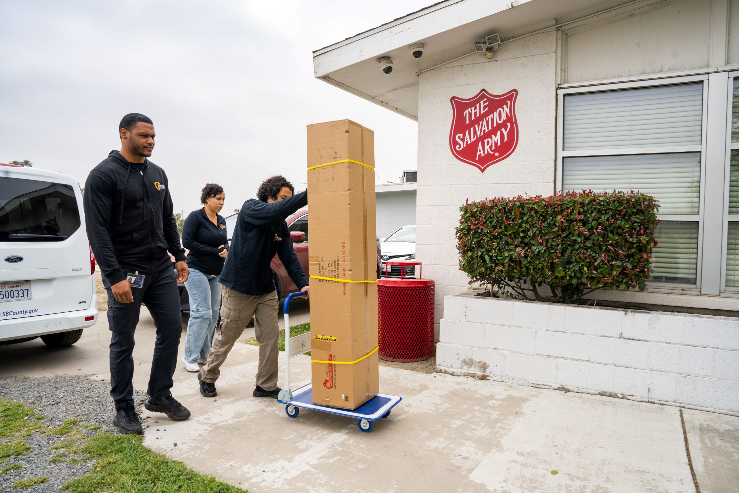 Three individuals transport a bed bug treatment unit on a cart outside of the Salvation Army building.