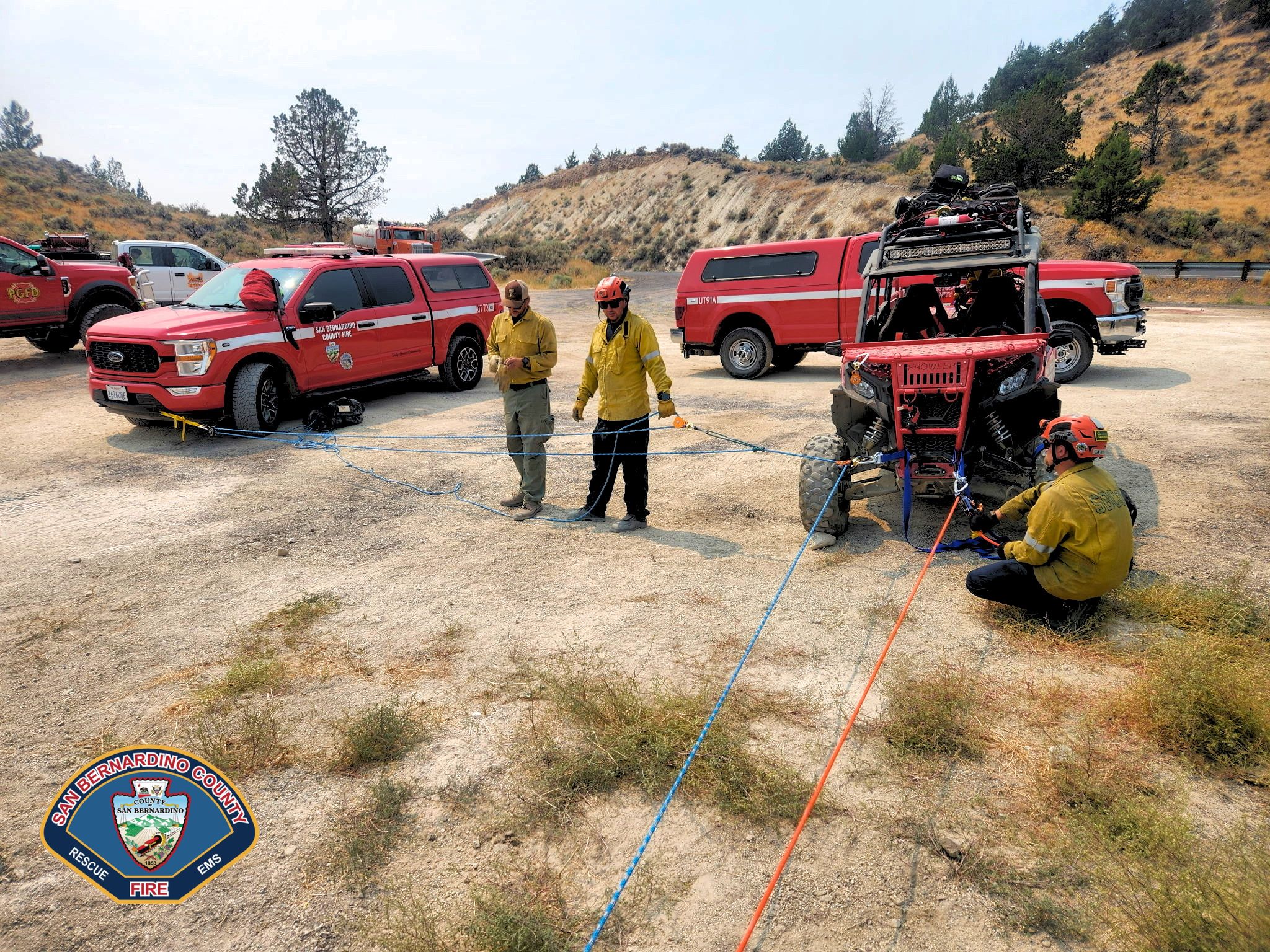 San Bernardino County Fire crew rigging rope lines around an all-terrain rescue vehicle during a rescue training exercise outdoors.