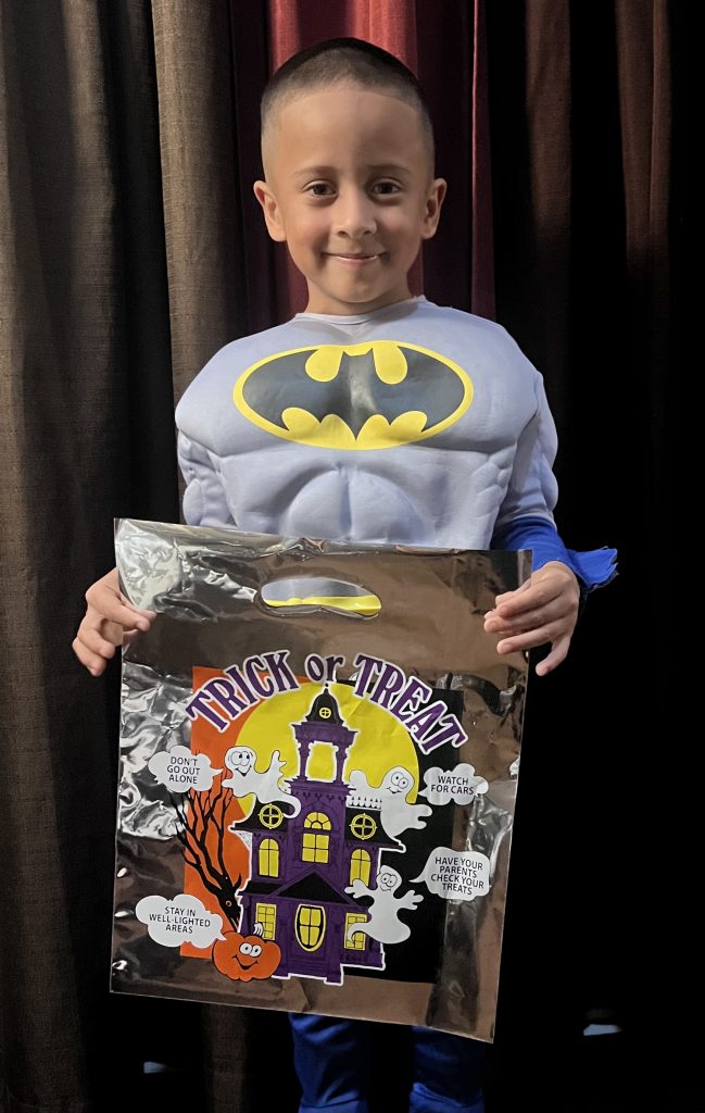 Young child in Batman costume smiles and holds a reflective bag.