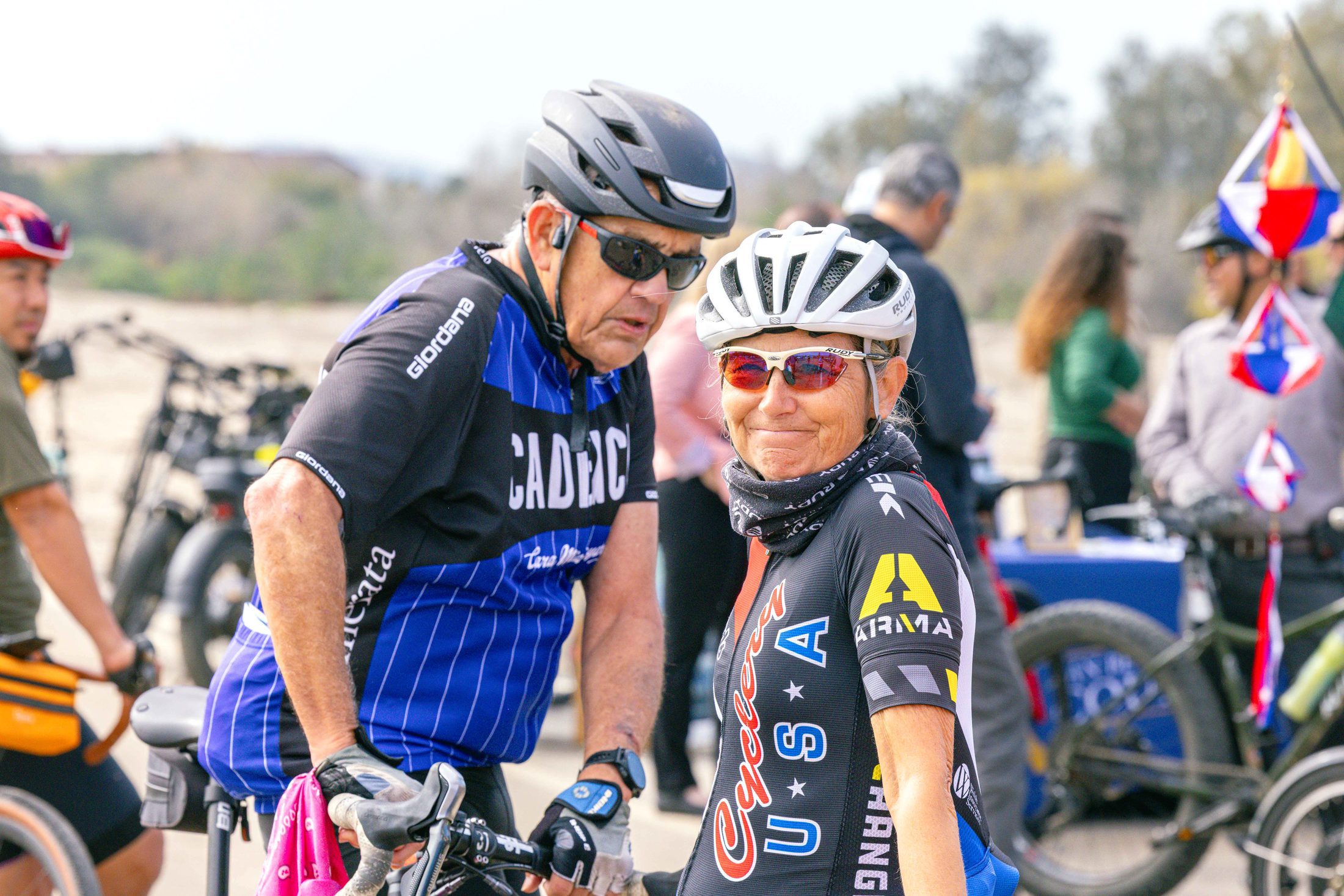 A male and female dressed in bicycling race gear and helmets stand with their bikes on the Santa Ana River Trail in San Bernardino.