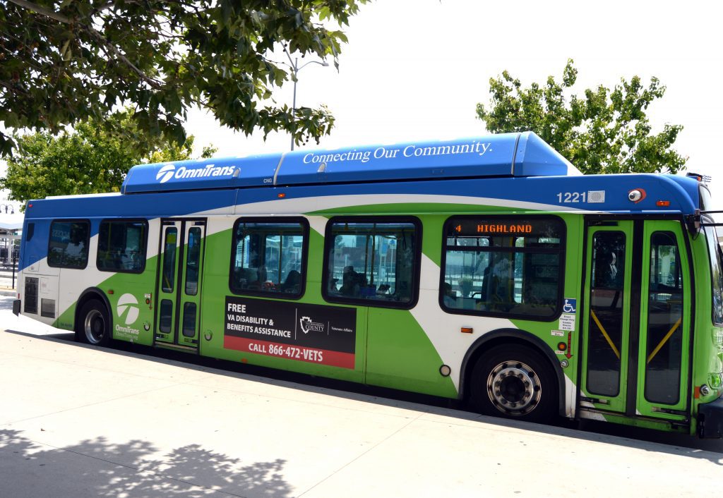 A black and red ad for Veterans Affairs appears on the side of a green and white OmniTrans bus with white text that says, “free Veterans Affairs disability and benefits assistance, call 866-472-8387.”