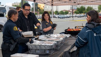 Probation staff and partners serve hot meals under a canopy during a community outreach event.
