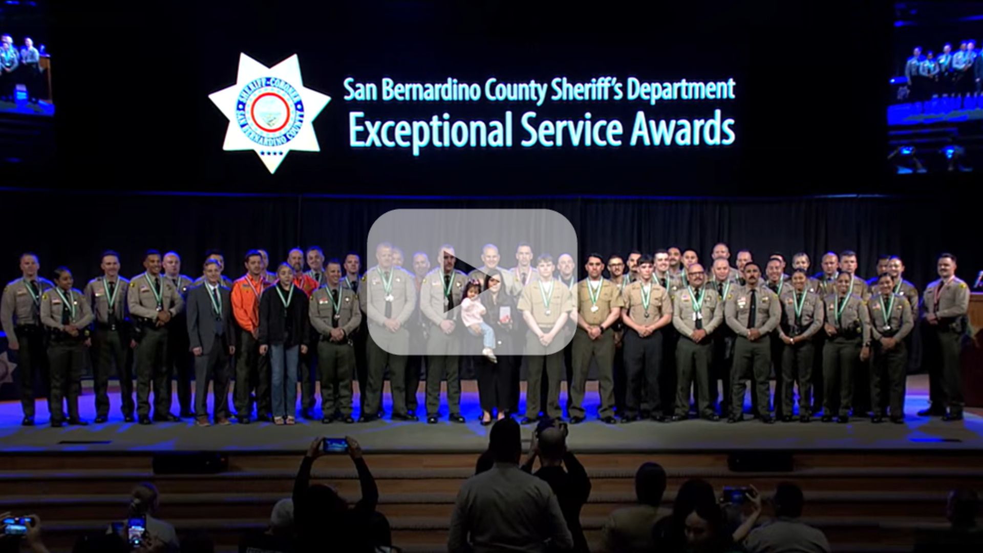 Medal-wearing deputies and individuals on stage at awards ceremony. Text: “San Bernardino County Sheriff’s Department Exceptional Service Awards”