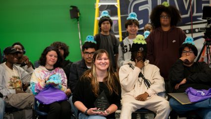 Teacher Lydia Lane poses with Film and Broadcasting students in front of a green screen classroom set.