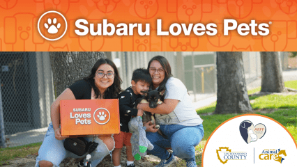 Subaru Loves Pets banner with two adults, a child, and a puppy outdoors. One holds a Subaru Loves Pets box, with County, ARFF, and Animal Care logos