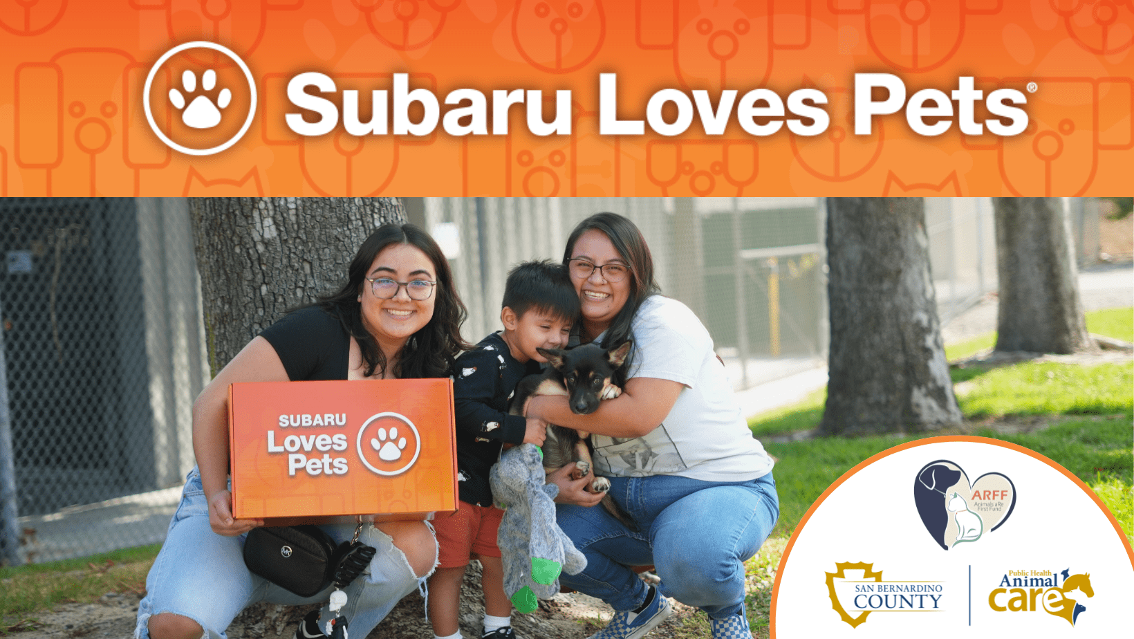 Subaru Loves Pets banner with two adults, a child, and a puppy outdoors. One holds a Subaru Loves Pets box, with County, ARFF, and Animal Care logos