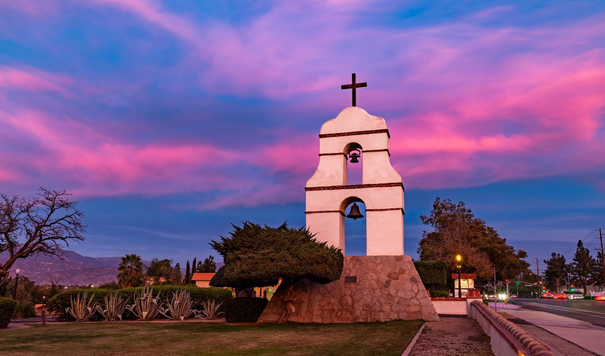 An image of a historic bell tower with a cross on top taken at sunset.