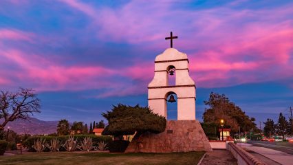 An image of a historic bell tower with a cross on top taken at sunset.