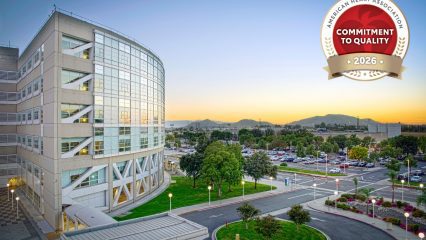 A hospital surrounded by a parking area and mountains in the distance. A badge is displayed in the corner, labeled "American Heart Association Commitment to Quality 2026.”
