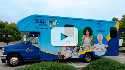 Parked Mobile Office with text, Support Starts Here, wp.sbcounty.gov/TAD and County logo. Images of dad and kids, woman cooking and senior with heart.