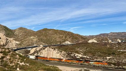 A BNSF freight train travels through a desert landscape, surrounded by hills and vegetation.