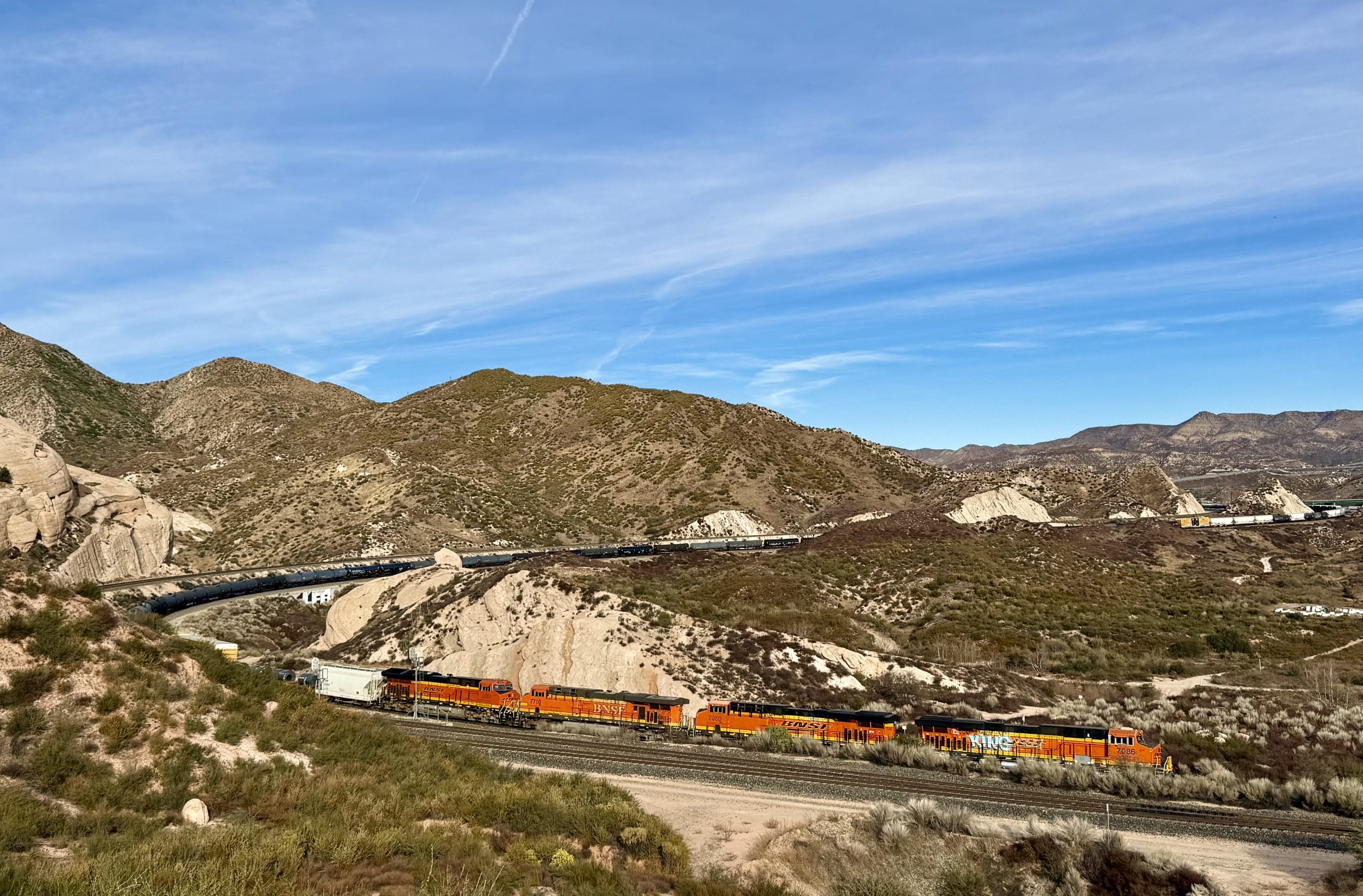 A BNSF freight train travels through a desert landscape, surrounded by hills and vegetation.