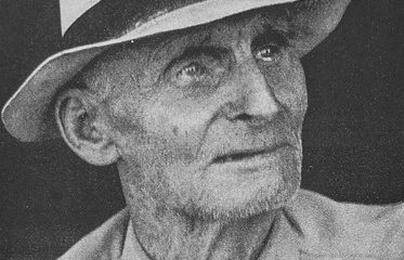 A black and white image of an older adult with a hat and a collared shirt.