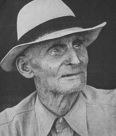 A black and white image of an older adult with a hat and a collared shirt.