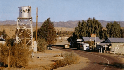 A photo of Earp, CA with a water tower, a few buildings and vehicles.