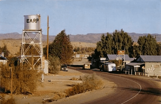 A photo of Earp, CA with a water tower, a few buildings and vehicles.