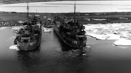 Two navy ships are docked side by side. The ship on the left displays the number 822 and the ship on the right displays 1110.