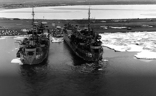 Two navy ships are docked side by side. The ship on the left displays the number 822 and the ship on the right displays 1110.