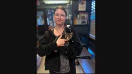 A woman standing inside an animal shelter, holding a small kitten.