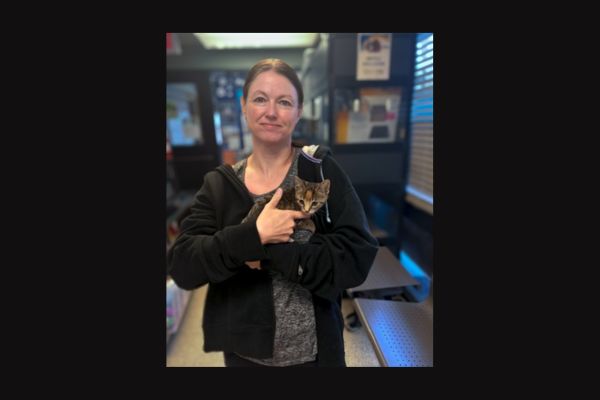 A woman standing inside an animal shelter, holding a small kitten.