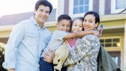 A happy military family hugging each other in front of a house.