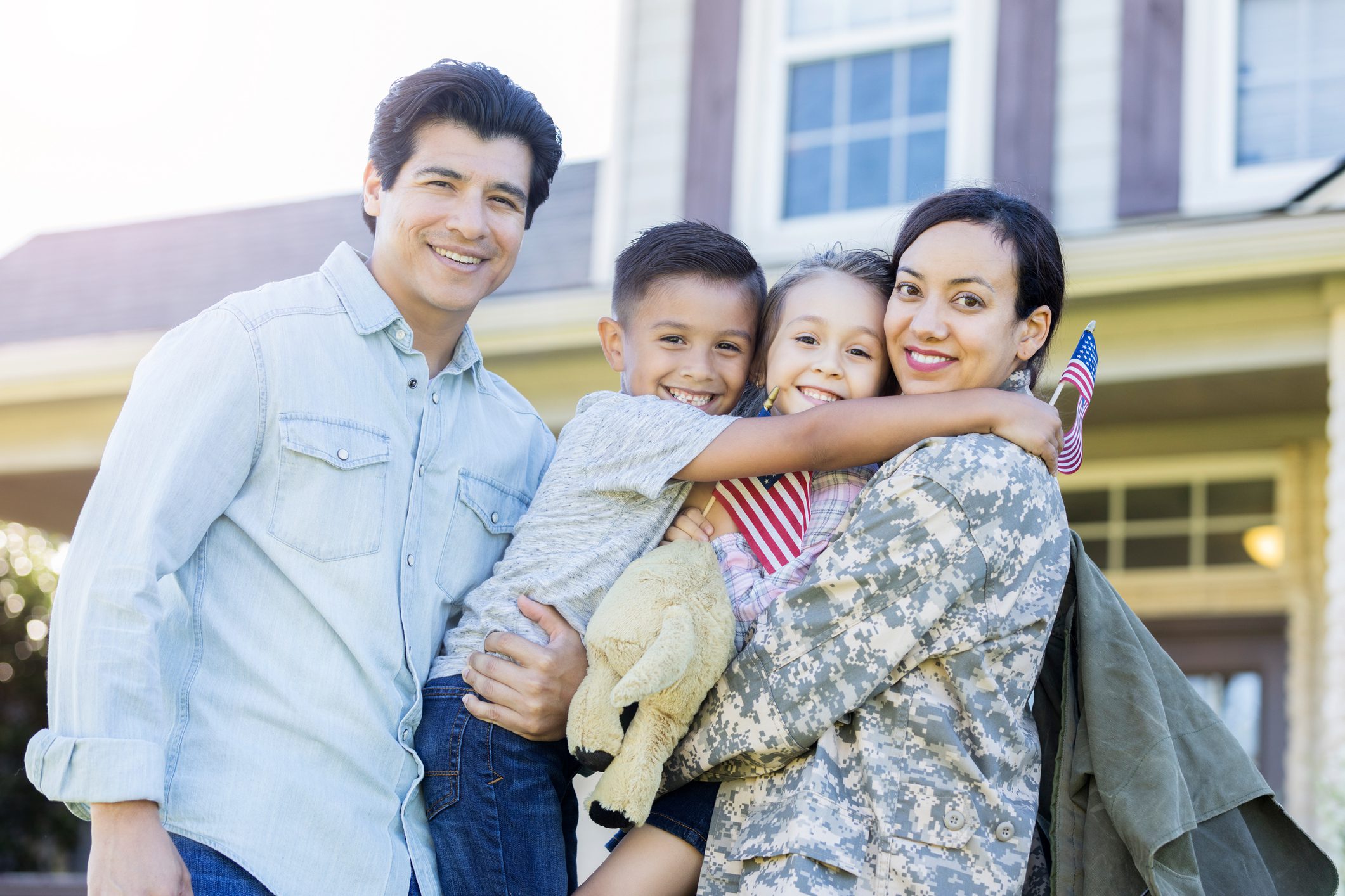 A happy military family hugging each other in front of a house.
