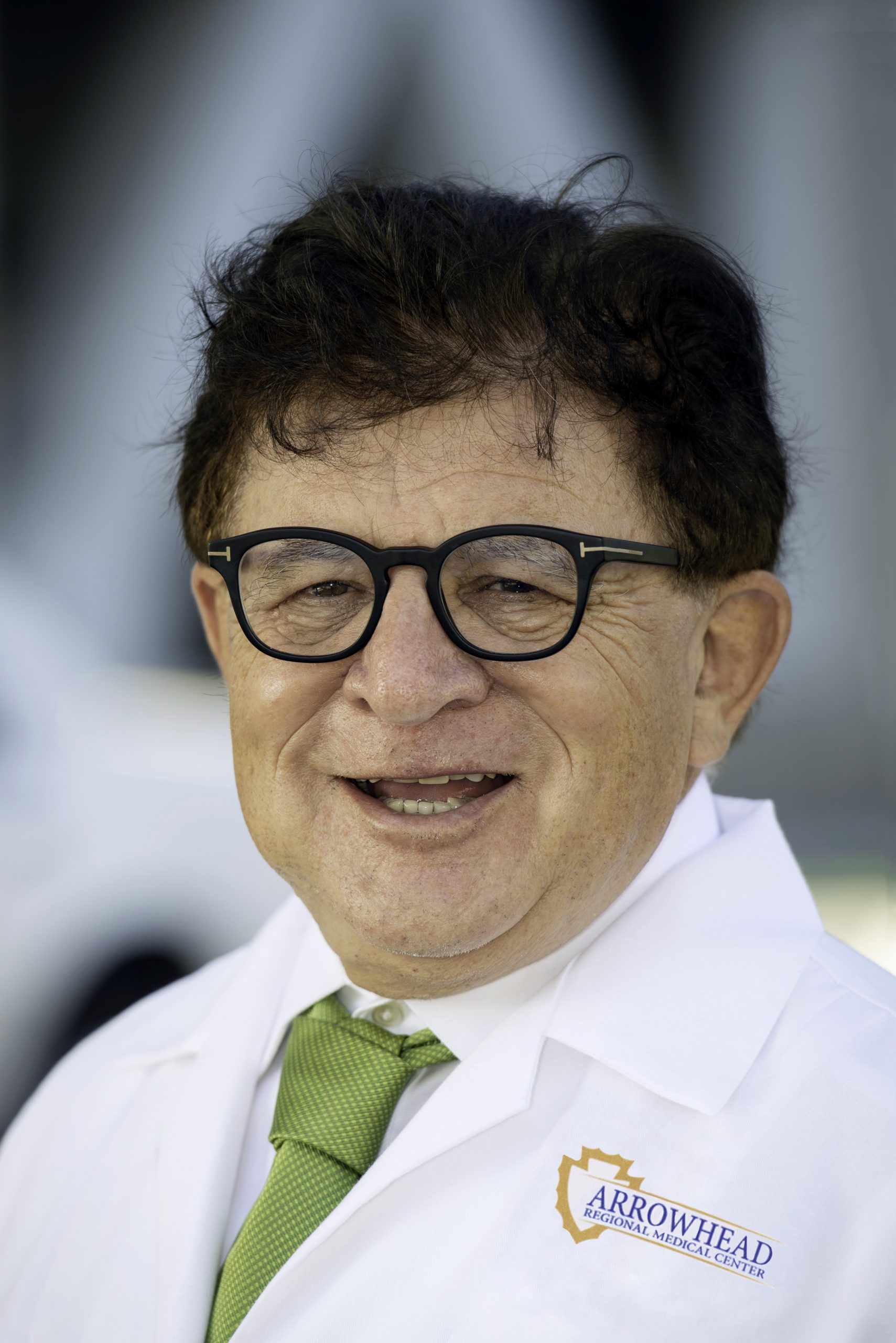 A male doctor wearing a white laboratory coat with the Arrowhead Regional Medical Center logo smiles at the camera.