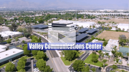 Aerial view of the campus with parking canopies and surrounding neighborhood. Text: “Valley Communications Center” with video play button.