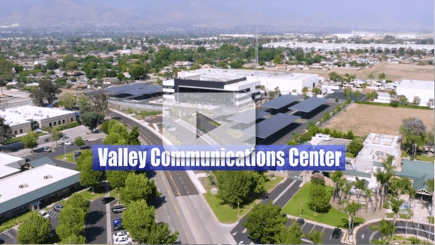 Aerial view of the campus with parking canopies and surrounding neighborhood. Text: “Valley Communications Center” with video play button.