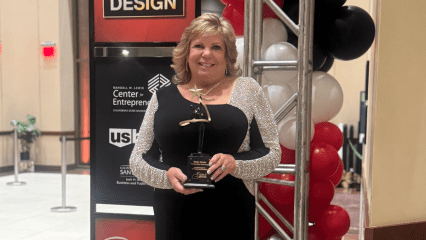 A smiling woman in a black dress holds a star-shaped award while standing beside red, white and black balloons at an event.
