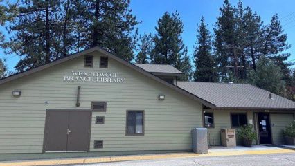 A light green library building with Wrightwood Branch Library on the facade surrounded by tall pine trees.
