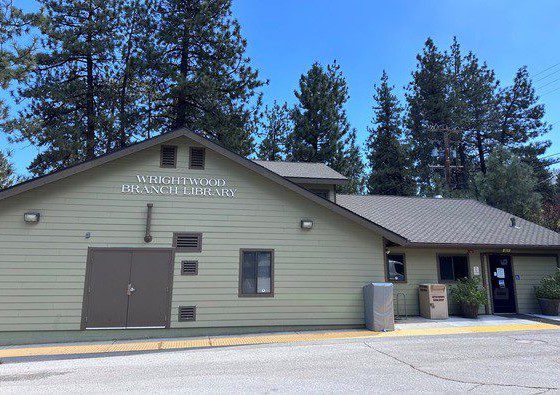 A light green library building with Wrightwood Branch Library on the facade surrounded by tall pine trees.