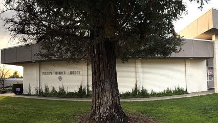 A beige building with a tall clock tower stands under a clear blue sky. Two flags are in front. The scene is calm and orderly, conveying a civic atmosphere.