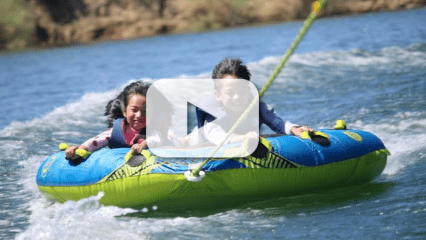 Two young children have fun on a green and blue raft in the water.