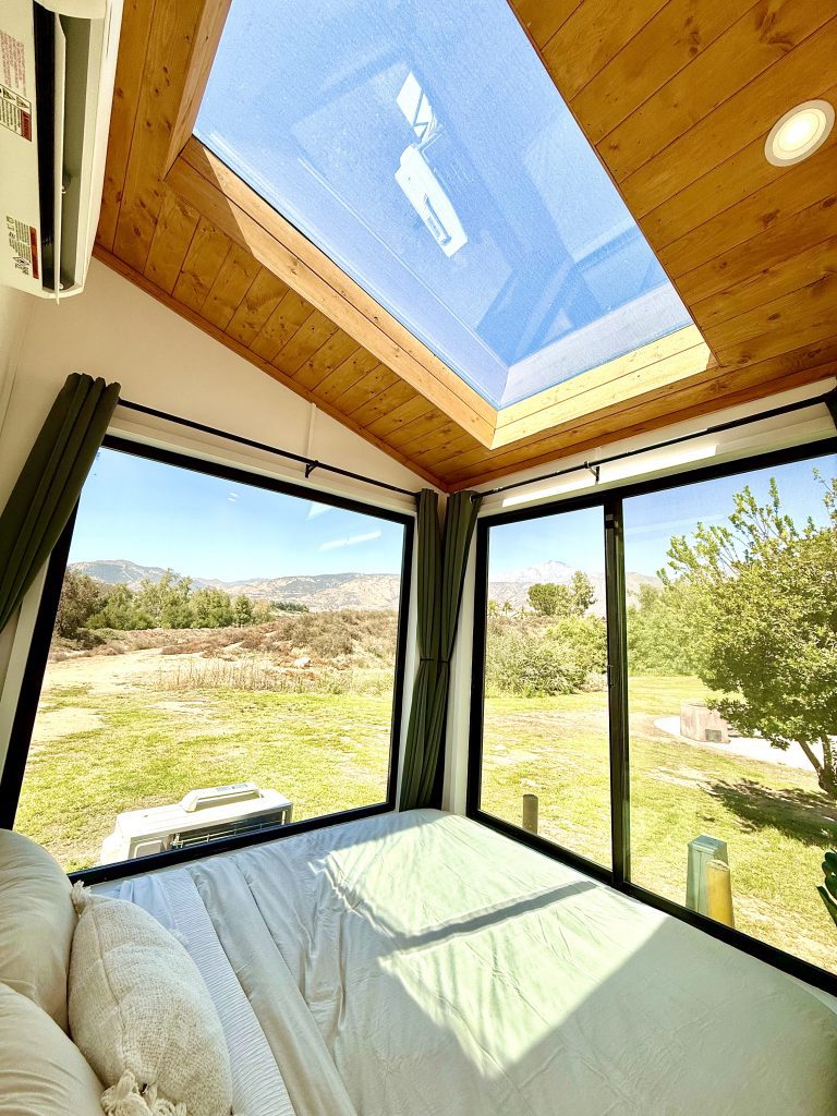 Interior featuring a bed surrounded by floor-to-ceiling windows with a large skylight overlooking mountains, trees, and open parkland space.
