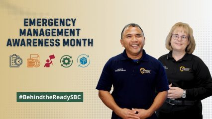 Two County employees smile beside text reading “Emergency Management Awareness Month” and #BehindtheReadySBC.