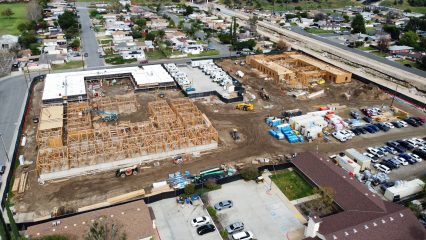View of a construction site with multiple building frames and equipment. Residential neighborhood surrounds the site.