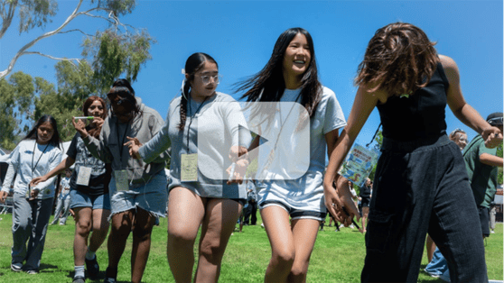 Video thumbnail showing teens participating in an outdoor team‑building activity with a play button overlay.