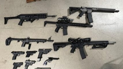 A collection of firearms is displayed on the ground, including various rifles and handguns.