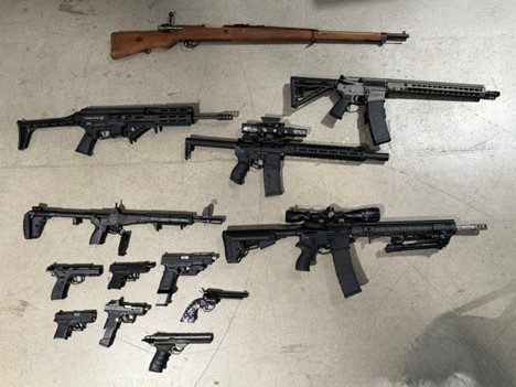 A collection of firearms is displayed on the ground, including various rifles and handguns.