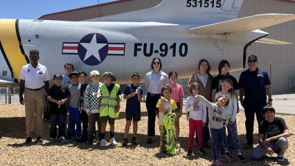 Group of students and adults posing in front of a vintage jet.