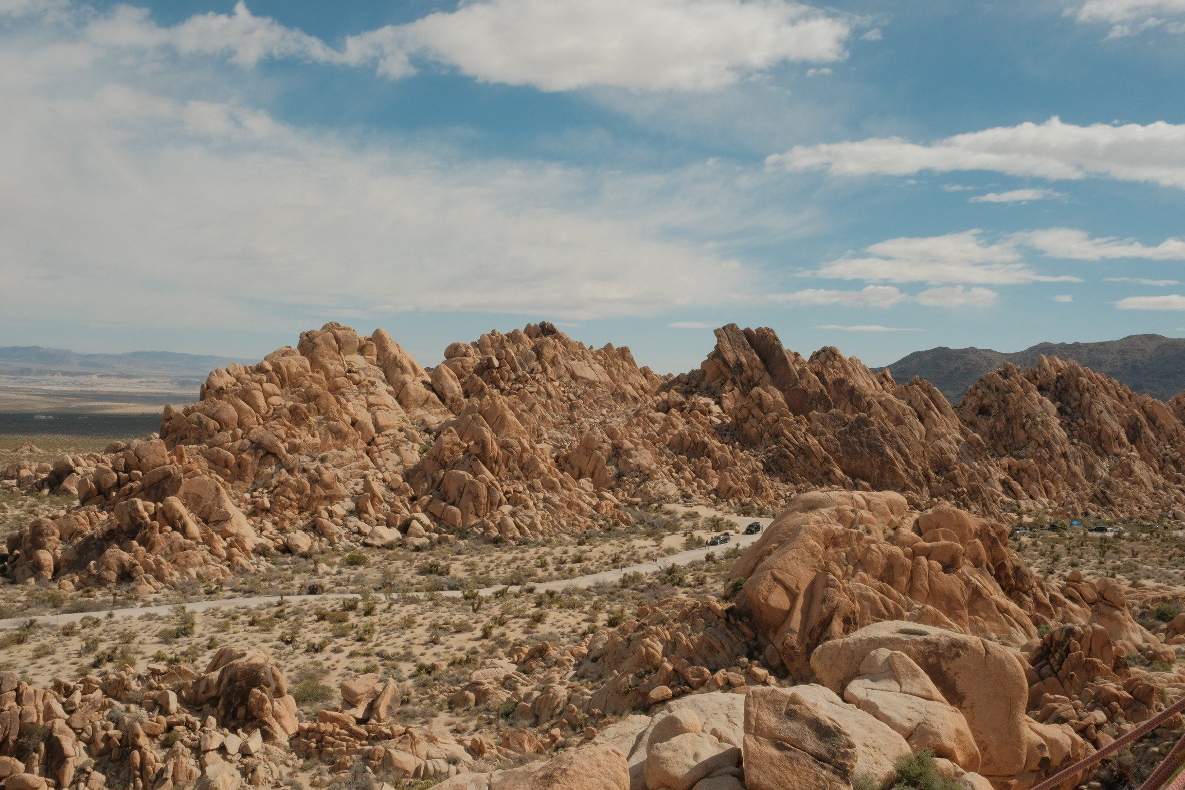 A desert landscape with rocky hills and scattered vegetation under a partly cloudy sky.