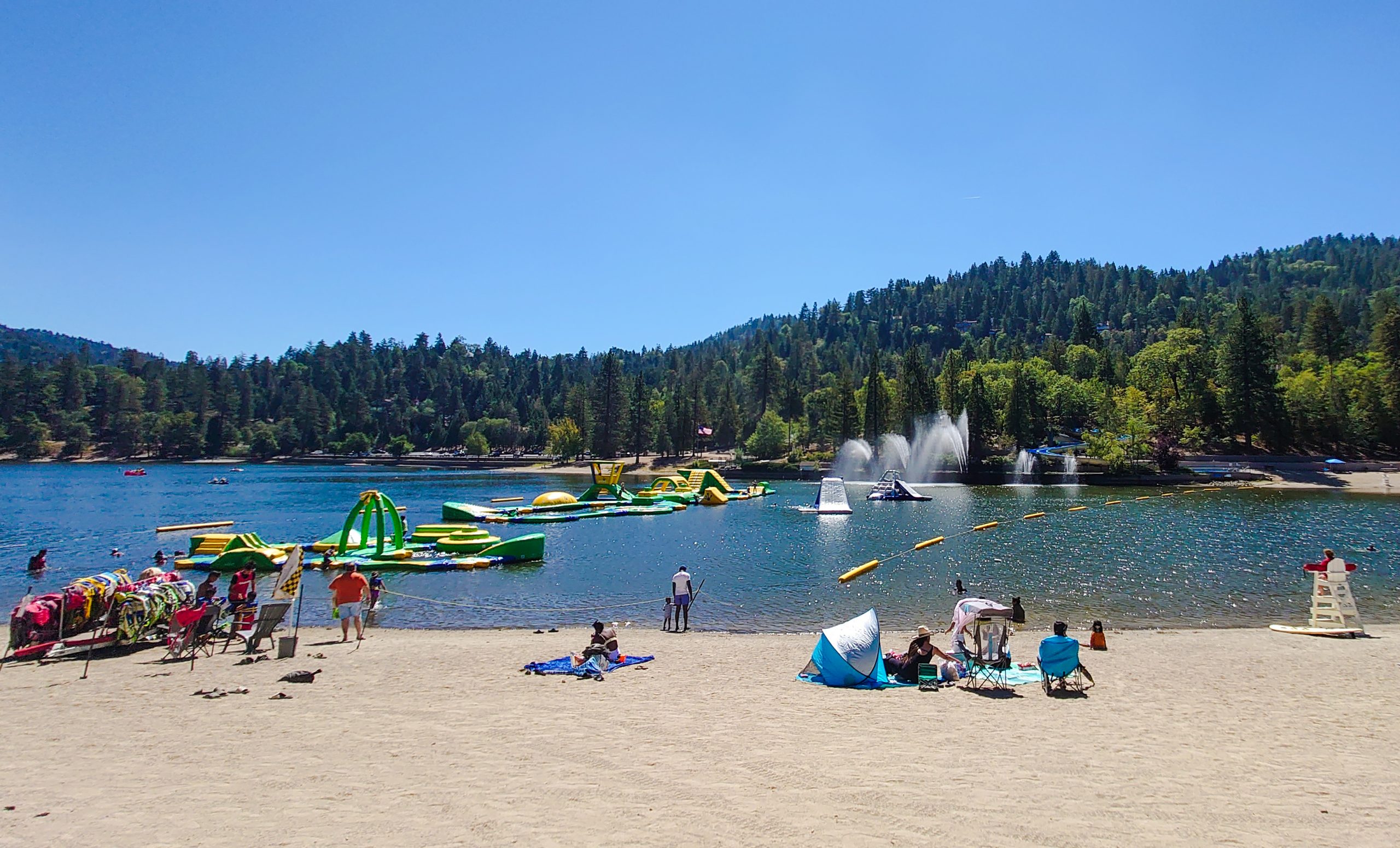 View of a lake featuring an inflatable water park and several visitors relaxing on the shore.