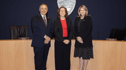 Baca, Jr., Decker, and Rowe pose in the Government Center’s Covington Chambers, standing in front of the county seal.